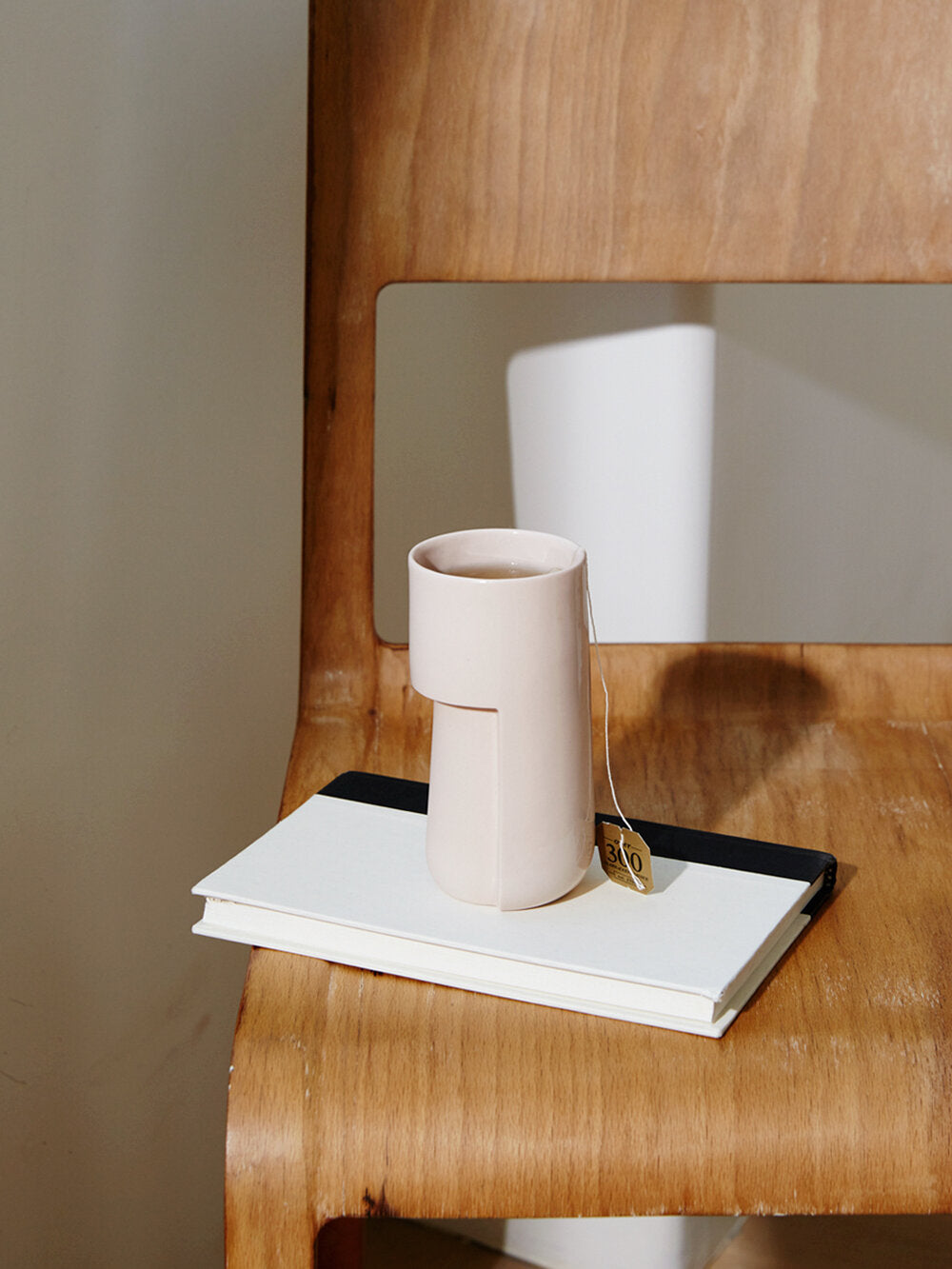 Hiball ceramic mug in Blush pink color containing tea sits atop a wooden chair 