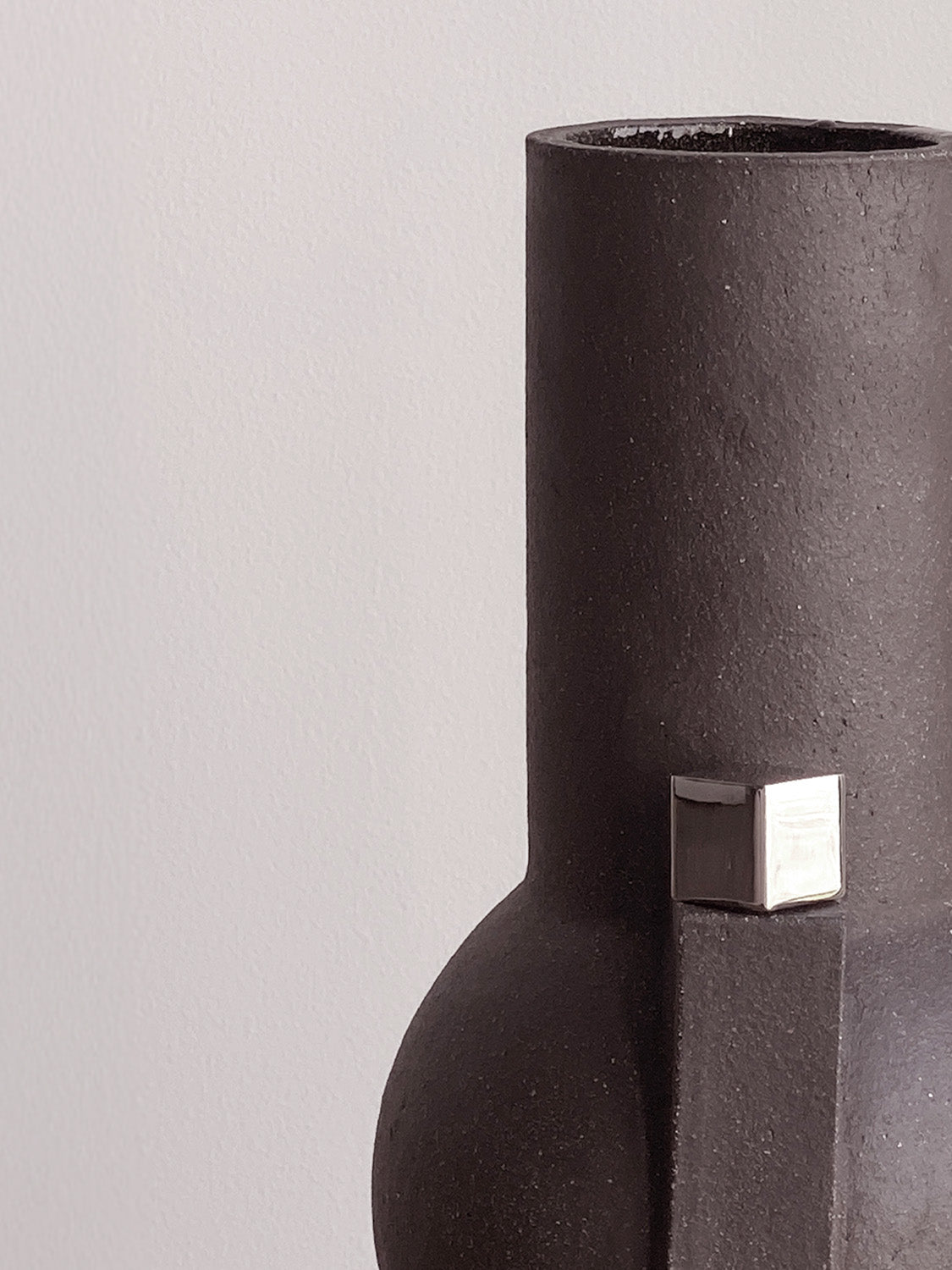 Black vase with a silver square accent on a light gray background