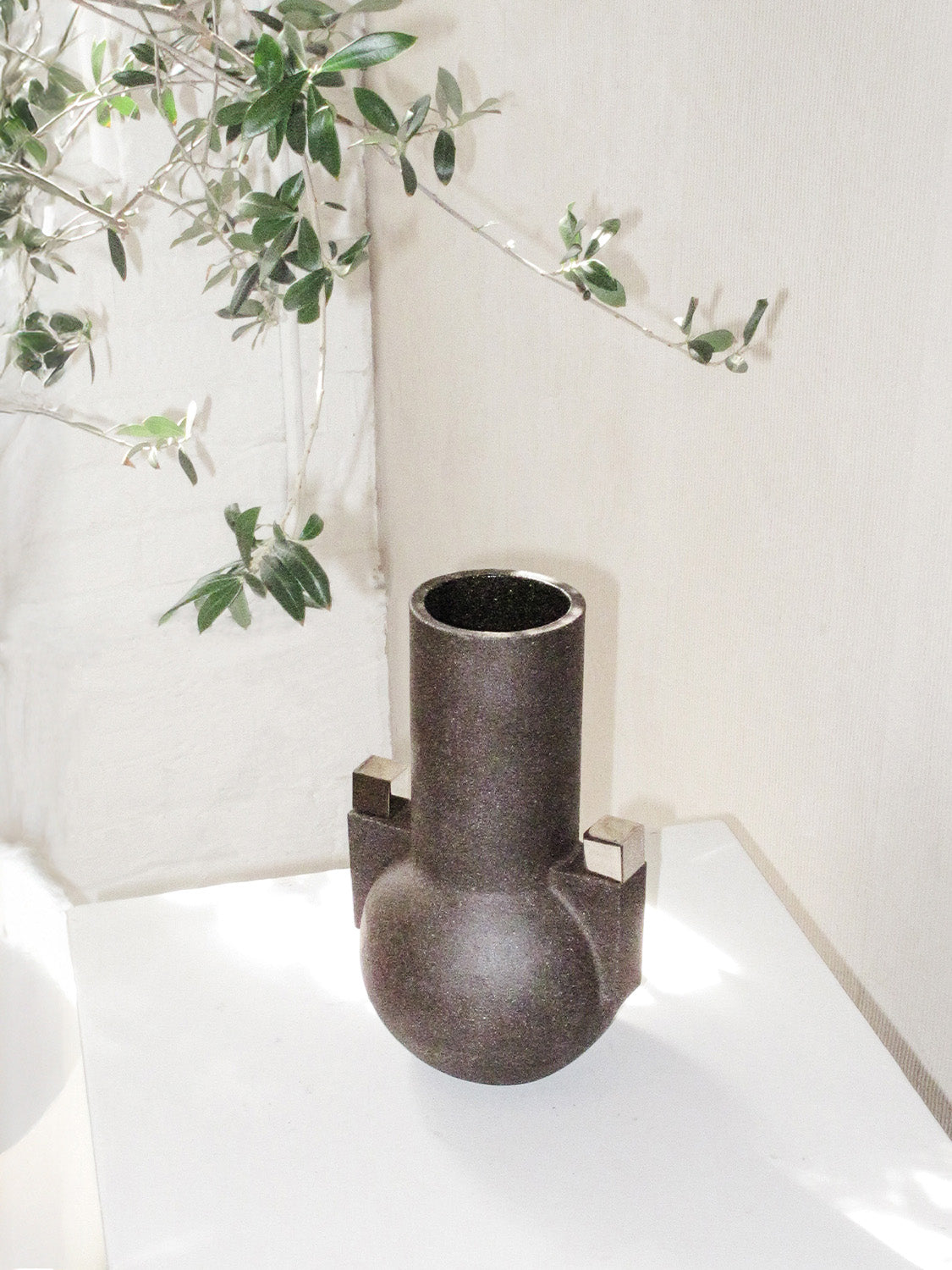 Decorative vase on a white surface with greenery in the background