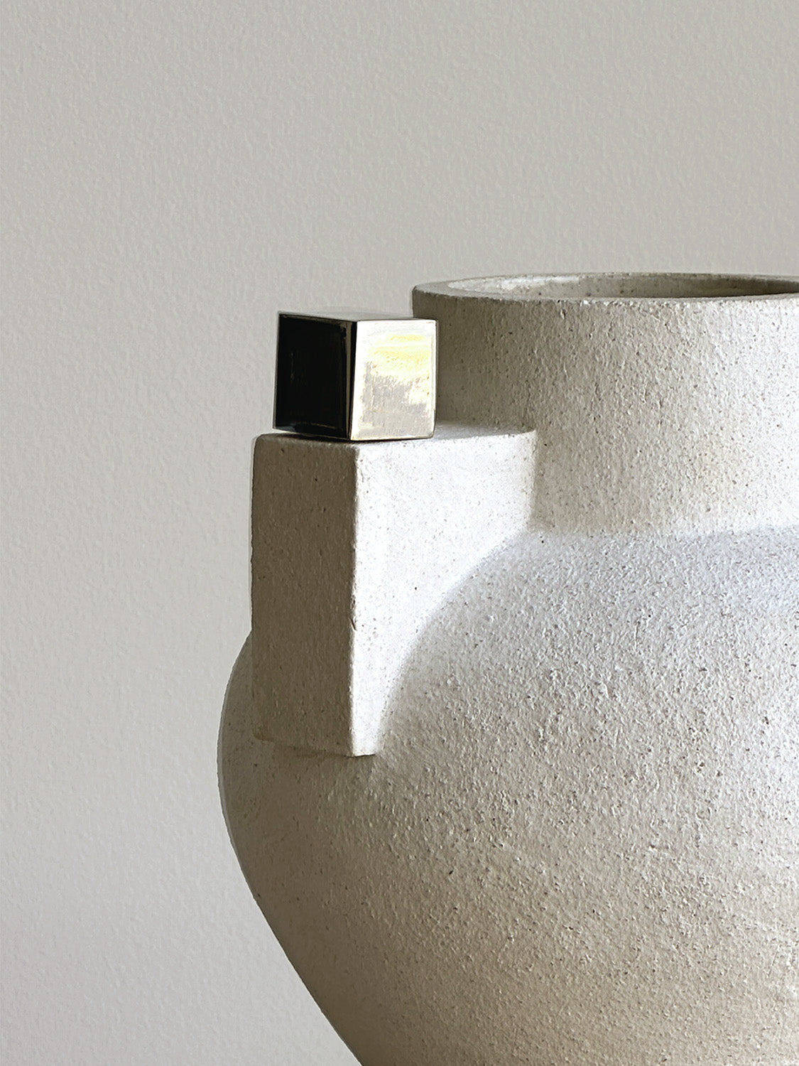 Close-up of a textured ceramic vase with a metallic cube on a light gray background