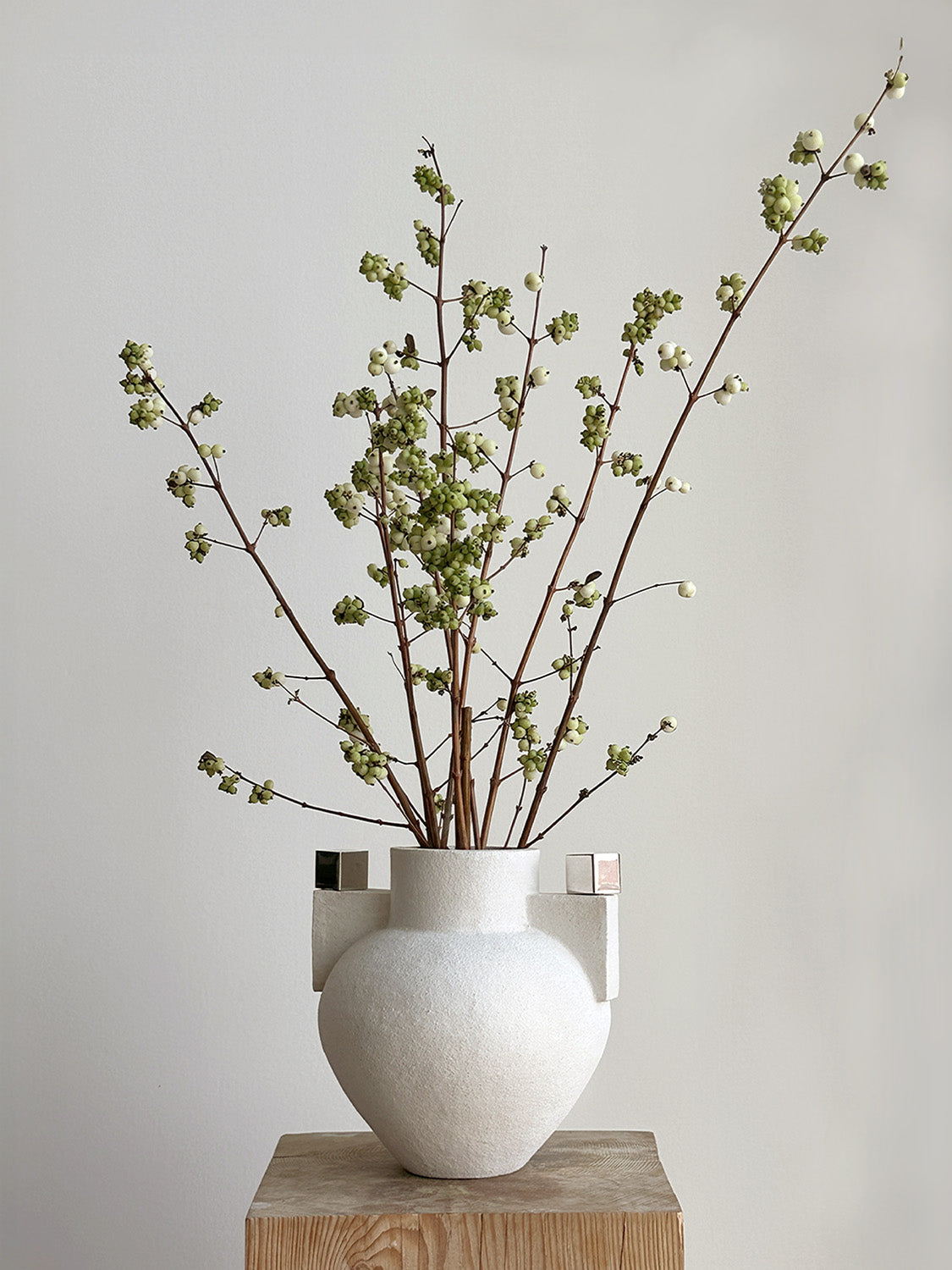 White vase with branches on a wooden block against a plain background