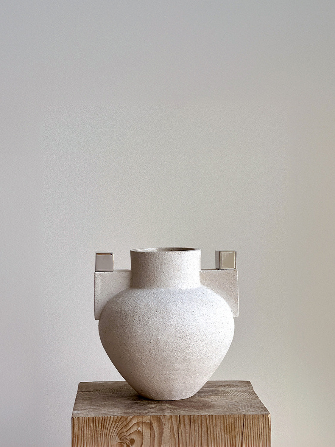 White textured vase on a wooden pedestal against a plain wall