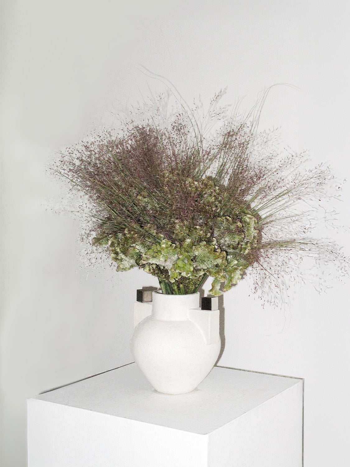 White vase with dried flowers on a white surface against a light gray background