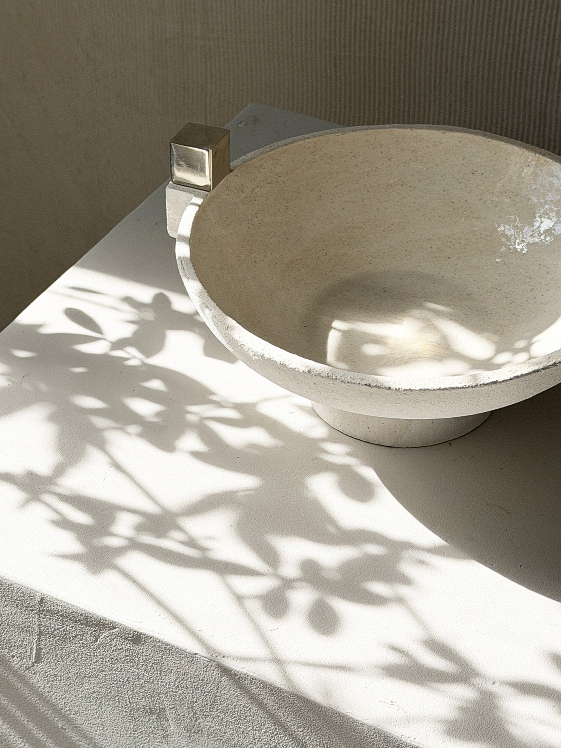 Ceramic bowl with metallic accents on a light surface with plant shadows