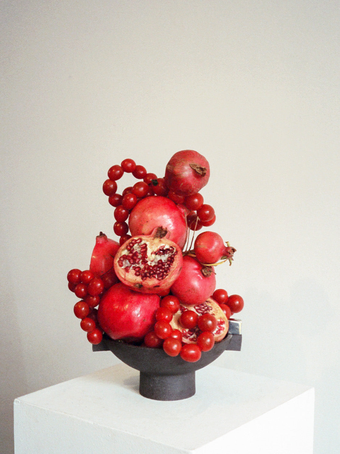 Fruit arrangement with pomegranates and red berries on a white surface