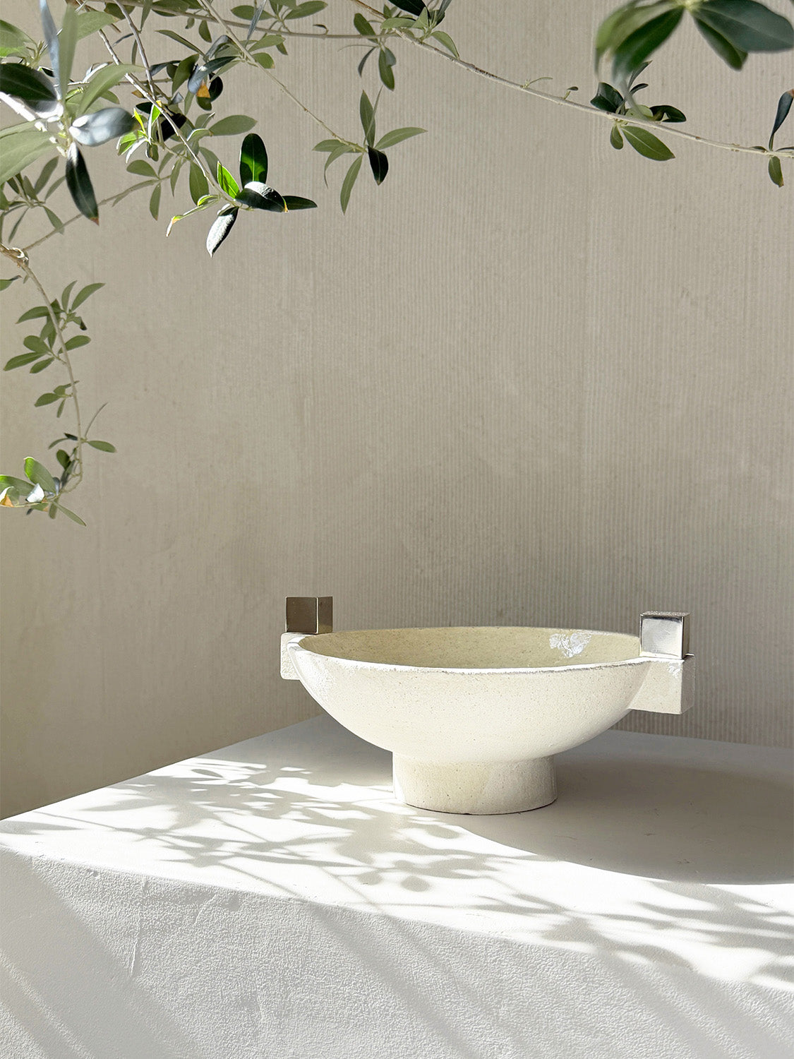 White freestanding bathtub against a beige wall with sunlight casting shadows on a white surface.