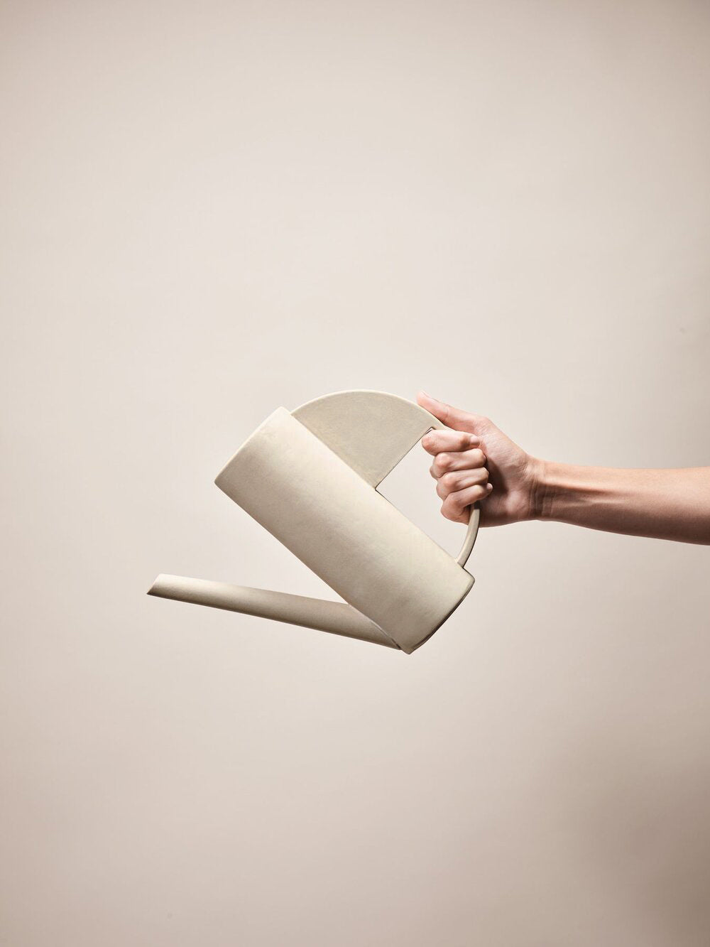 Pouring from sandy sculptural watering can. Made from stoneware 