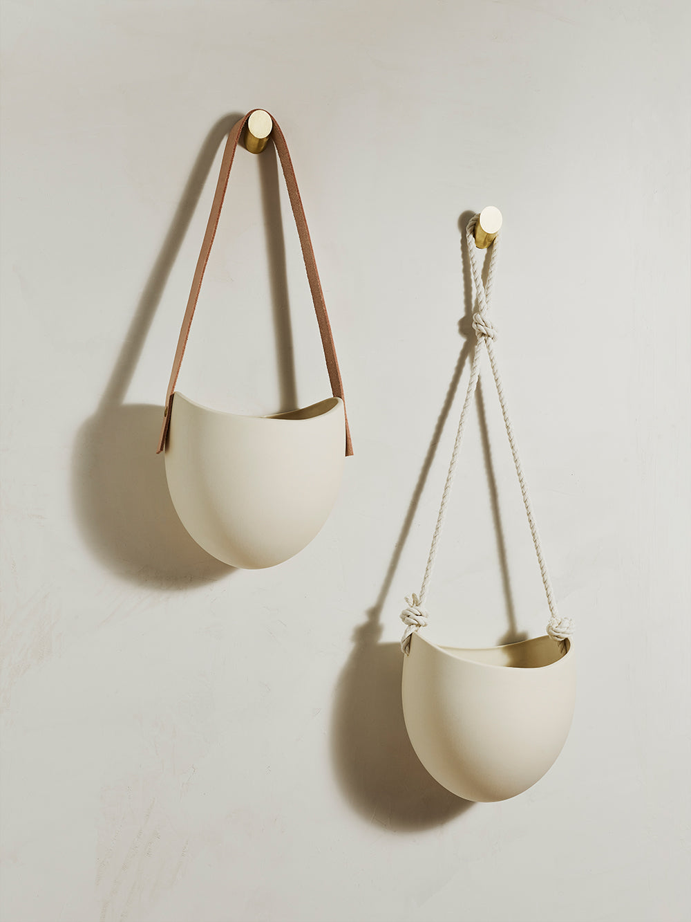 Two wall hanging planters side by side, one with leather hanger and one with rope